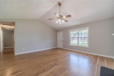 Spare room featuring ceiling fan, wood finished floors, a textured ceiling, baseboards, and lofted ceiling
