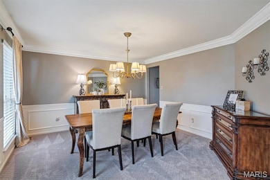 Carpeted dining area featuring ornamental molding, a wainscoted wall, a decorative wall, and a chandelier