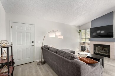 Living room with vaulted ceiling, light wood-type flooring, a textured ceiling, and a fireplace