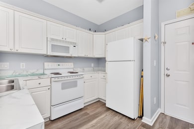 Kitchen featuring white appliances, light countertops, light wood finished floors, and white cabinets