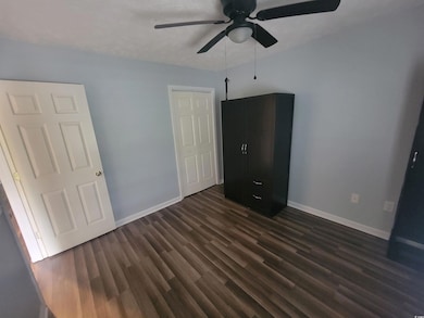 Unfurnished bedroom featuring dark wood-style floors, baseboards, and a ceiling fan