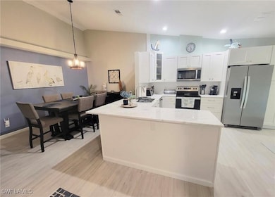 Kitchen featuring appliances with stainless steel finishes, a peninsula, glass insert cabinets, hanging light fixtures, and white cabinets