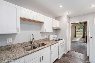 Kitchen with white appliances, white cabinetry, dark wood finished floors, light stone counters, and under cabinet range hood