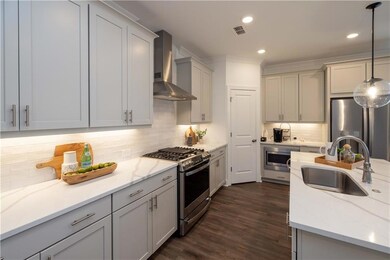 Kitchen with wall chimney exhaust hood, stainless steel appliances, a sink, tasteful backsplash, and decorative light fixtures