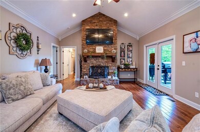 Living area featuring a ceiling fan, wood finished floors, lofted ceiling, a stone fireplace, and ornamental molding