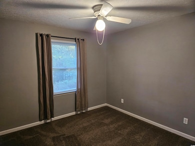 Unfurnished room featuring a textured ceiling, dark carpet, and ceiling fan