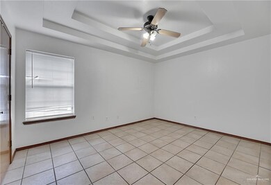 Empty room featuring ceiling fan, light tile floors, and a raised ceiling
