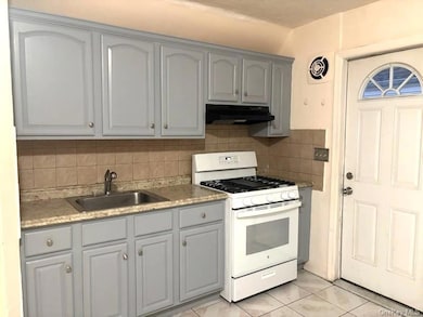 Kitchen featuring gray cabinets, white range with gas stovetop, tasteful backsplash, light tile patterned floors, and under cabinet range hood