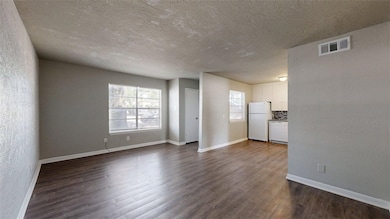 Unfurnished living room with a textured wall, dark wood finished floors, and a textured ceiling