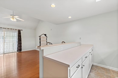 Kitchen with a peninsula, a ceiling fan, lofted ceiling, white cabinets, and light countertops