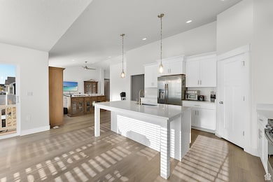 Kitchen with a kitchen island with sink, white cabinetry, appliances with stainless steel finishes, decorative light fixtures, and a kitchen bar