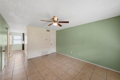 Tiled empty room with a textured ceiling and a ceiling fan