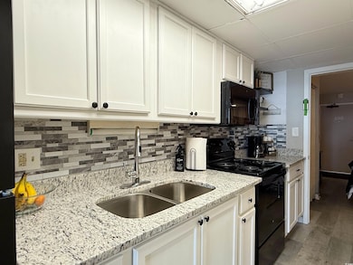 Kitchen with black appliances, a sink, white cabinetry, light wood finished floors, and backsplash
