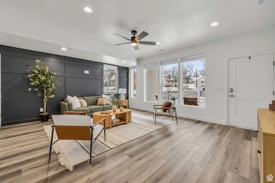 Living area featuring ceiling fan, light wood-style flooring, a decorative wall, and recessed lighting