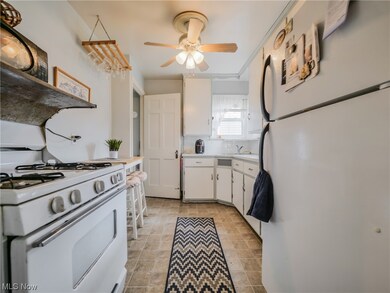 Kitchen with white appliances, light tile flooring, white cabinets, and ceiling fan