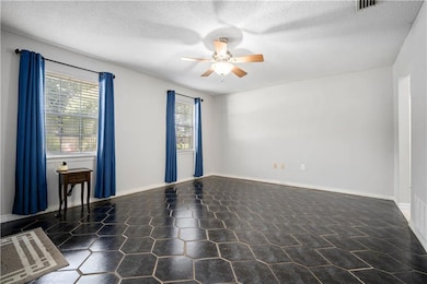 Empty room featuring ceiling fan, healthy amount of natural light, and a textured ceiling