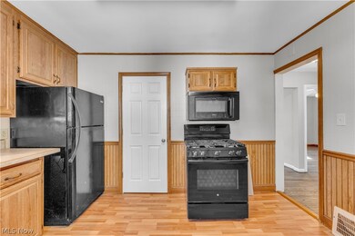 Kitchen with light hardwood / wood-style floors, crown molding, and black appliances