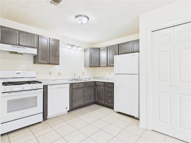 Kitchen featuring white appliances, light countertops, dark brown cabinets, light tile patterned floors, and under cabinet range hood