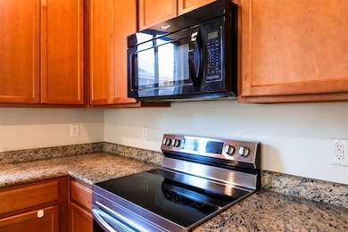 Kitchen with electric stove, black microwave, brown cabinets, and dark stone counters