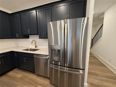 Kitchen with appliances with stainless steel finishes, a sink, light stone countertops, light wood-style flooring, and decorative backsplash
