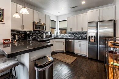 Kitchen with appliances with stainless steel finishes, a peninsula, dark wood-style floors, a breakfast bar area, and pendant lighting