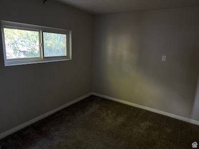 Unfurnished room featuring dark carpet and baseboards