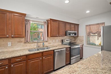 This kitchen features elegant granite countertops, stainless steel appliances, and rich wooden cabinetry. It has ample natural light from two windows.