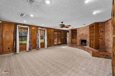 Unfurnished living room featuring a textured ceiling, wood walls, a brick fireplace, light colored carpet, and ceiling fan