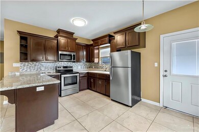 Kitchen with appliances with stainless steel finishes, a peninsula, dark brown cabinets, open shelves, and decorative backsplash