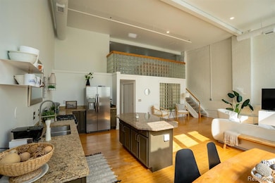 Kitchen featuring light stone counters, stainless steel refrigerator with ice dispenser, beam ceiling, light wood-style flooring, and a towering ceiling