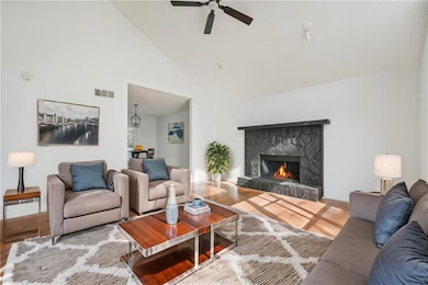 Living area with visible vents, high vaulted ceiling, wood finished floors, a fireplace, and ceiling fan
