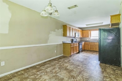 Kitchen with electric range, freestanding refrigerator, a chandelier, stainless steel microwave, and brown cabinetry