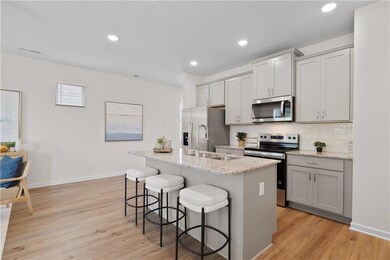 Kitchen featuring stainless steel appliances, gray cabinets, backsplash, a breakfast bar area, and light stone countertops