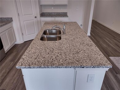 Kitchen with a kitchen island with sink, white cabinetry, light stone countertops, and dark wood finished floors