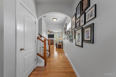 Hallway with arched walkways, light wood finished floors, and stairs
