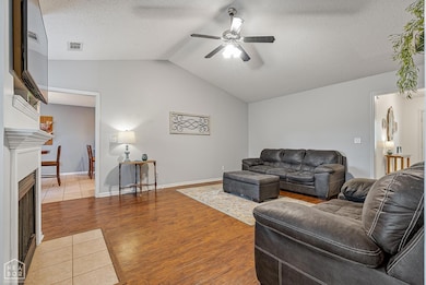 Spacious living area with vaulted ceilings, rich wood flooring, and a cozy fireplace as the focal point. Large windows allow natural light to fill the space, creating a warm and inviting atmosphere.