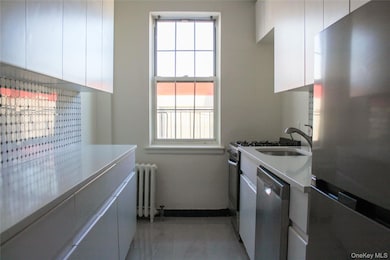 Kitchen with appliances with stainless steel finishes, radiator heating unit, white cabinetry, and light stone countertops
