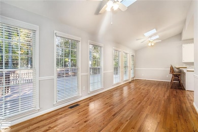 Unfurnished living room featuring lofted ceiling, ceiling fan, light wood-style flooring, and a skylight