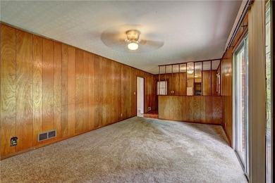 Unfurnished living room featuring carpet floors, ceiling fan, plenty of natural light, and wooden walls