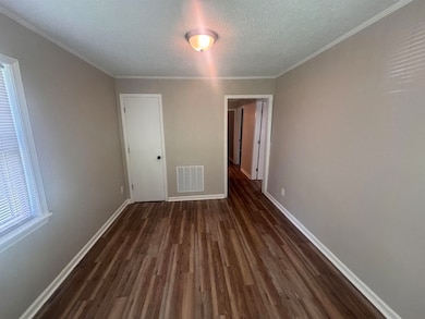 Empty room with dark wood finished floors, a textured ceiling, baseboards, and crown molding