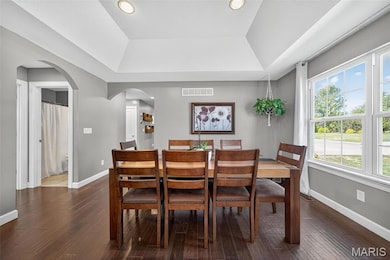 Dining area featuring arched walkways, dark wood finished floors, a raised ceiling, and recessed lighting