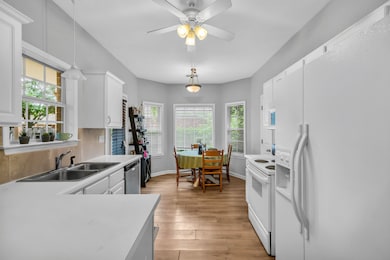 Kitchen with white appliances, a sink, light countertops, white cabinets, and light wood-type flooring