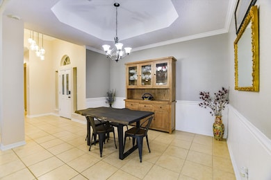 Dining space featuring a tray ceiling, light tile patterned floors, crown molding, and a chandelier