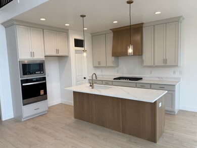 Kitchen featuring stainless steel appliances, light stone counters, recessed lighting, a kitchen island with sink, and light wood-style floors