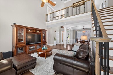 Living room featuring ornamental molding, wood finished floors, ceiling fan, stairway, and a high ceiling