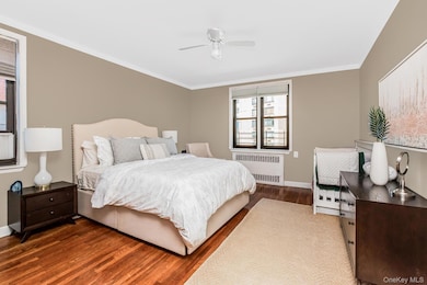 Bedroom featuring ceiling fan, crown molding, radiator heating unit, baseboards, and wood finished floors