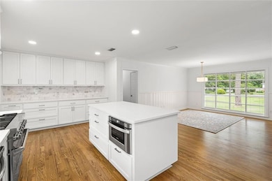 Kitchen with stainless steel appliances, light wood-style floors, wainscoting, white cabinets, and light countertops