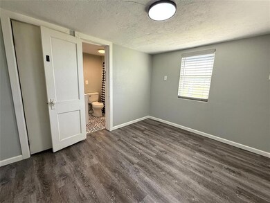 Unfurnished bedroom featuring a textured ceiling, dark wood-style floors, baseboards, and connected bathroom