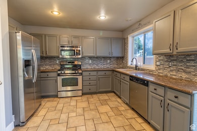 Kitchen featuring gray cabinets, appliances with stainless steel finishes, dark stone counters, tasteful backsplash, and recessed lighting
