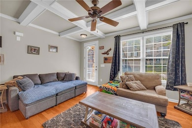Living room featuring coffered ceiling, a ceiling fan, light wood finished floors, beam ceiling, and crown molding